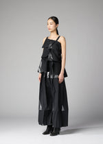 A woman with straight dark hair pulled back stands against a gray background wearing 132 5. ISSEY MIYAKE's No.1-1: a layered black recycled polyester top and wide-leg pants with shiny geometric accents, paired with black ankle boots.
