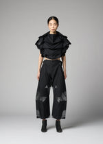 A woman stands against a plain background wearing the 132 5. ISSEY MIYAKE No.10-2 ensemble: a glamorous black ruffled crop top and wide-leg black pants with sheer geometric panels, crafted from recycled polyester, paired with black ankle boots.