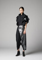 A woman poses against a gray background in the No.10-1 outfit by 132 5. ISSEY MIYAKE, featuring ruffled short sleeves, asymmetrical metallic silver accents on skirt-like pants, a foil-embellished jacket, and black ankle boots.