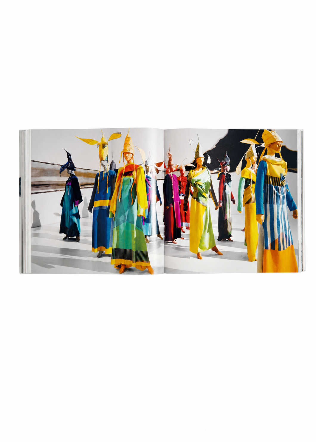 Zoomed view Models in vibrant, avant-garde ensembles and intricate headpieces—reflecting the bold creativity of Issey Miyake’s vision—pose against a pristine white backdrop adorned with abstract black and brown forms, as featured in the ISSEY MIYAKE (Limited Collectors Edition) by ISSEY MIYAKE BOOKS.
