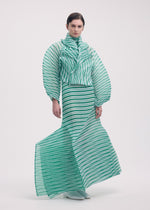 A person wears the ISSEY MIYAKE GENERIC STRIPES (HAND PLEATS) dress with green and white stripes, bold geometric patterns, handmade pleats, a high collar, structured sleeves, and a flared skirt against a plain light background.
