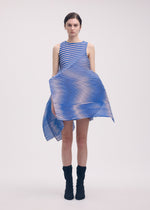 A person wears the ISSEY MIYAKE GENERIC STRIPES (MACHINE PLEATS) sleeveless blue and white striped dress with an asymmetrical flared hem, paired with black ankle boots, standing against a plain light background.