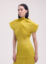 A person with straight dark hair wears the ISSEY MIYAKE GENERIC STRIPES (MACHINE PLEATS) dress, featuring pleated yellow fabric with black grid-like stripes, standing against a plain light background.
