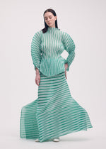A woman with long, straight dark hair stands against a plain background, wearing ISSEY MIYAKE’s GENERIC STRIPES (HAND PLEATS) set—green and white striped pleated top with matching skirt that flares dynamically at the hem.