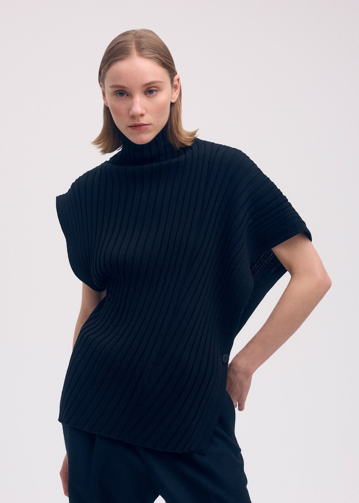 A woman with straight, shoulder-length light brown hair wears the ISSEY MIYAKE COTTON CASHMERE KNIT top and black pants, standing against a plain light background with one hand on her hip. view 5 of 5