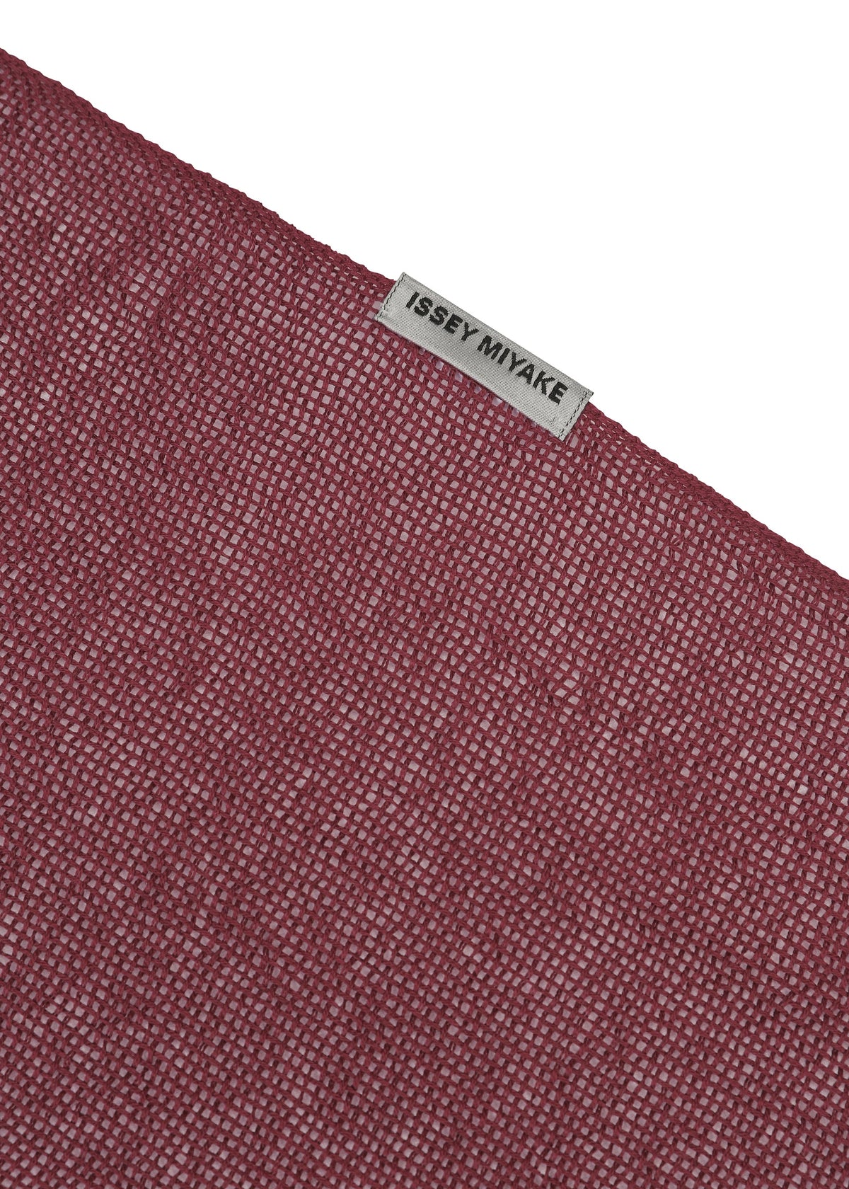 A close-up of the SLITS STOLE by ISSEY MIYAKE, featuring textured maroon cotton and a small gray ISSEY MIYAKE label sewn near the edge, set against a plain white background—ideal for versatile styling. view 5 of 7