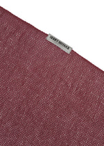 A close-up of the SLITS STOLE by ISSEY MIYAKE, featuring textured maroon cotton and a small gray ISSEY MIYAKE label sewn near the edge, set against a plain white background—ideal for versatile styling.