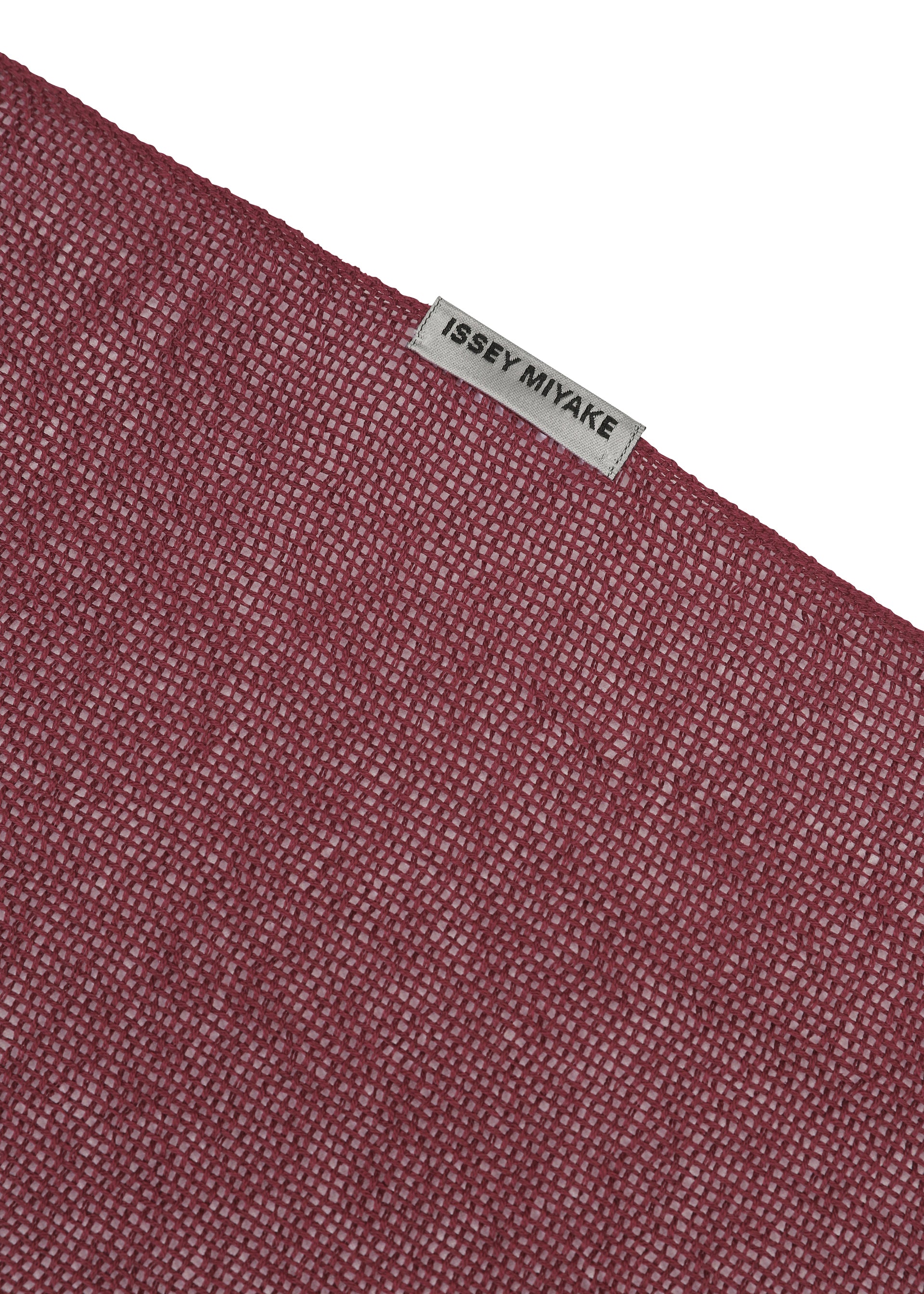 Zoomed view A close-up of the SLITS STOLE by ISSEY MIYAKE, featuring textured maroon cotton and a small gray ISSEY MIYAKE label sewn near the edge, set against a plain white background—ideal for versatile styling.