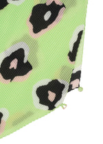 Close-up of the VERVE PLEATS STOLE by ISSEY MIYAKE, showing light green pleated fabric with diagonal ridges and abstract black, white, and pale pink hand-drawn leopard spots. Two small fabric-covered buttons appear at the bottom edge.