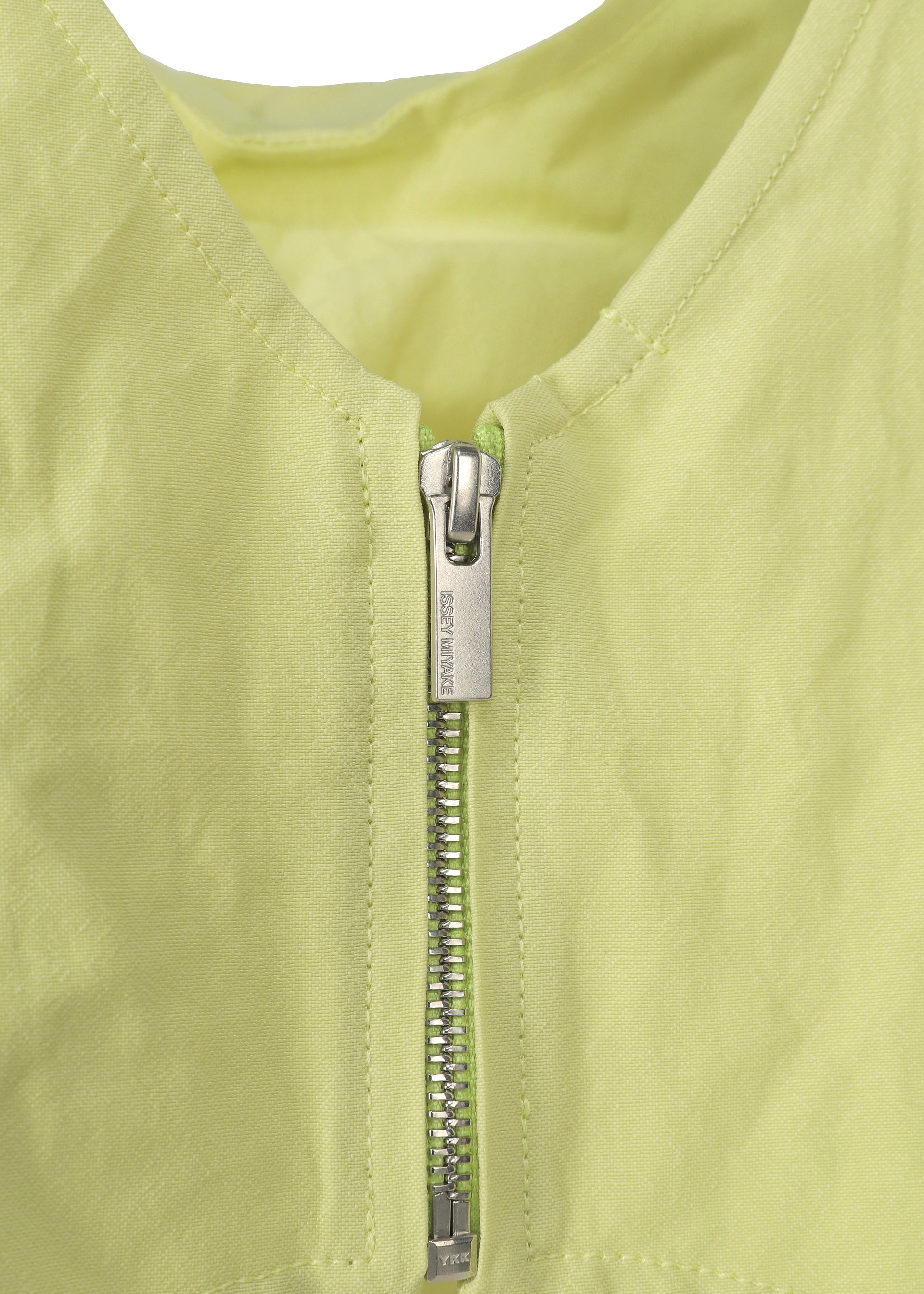 Zoomed view Close-up of a silver zipper with engraved text on the ISSEY MIYAKE PAPER BALLOON 2, a light yellow garment with subtle crinkled texture and matching lining. Visible stitching frames the neckline.