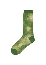 The OBSCURE SOCKS by ISSEY MIYAKE features a single green patterned sock with textured green and yellow shades, accented by subtle lamé threads, shown against a plain white background. - GREEN-HUED (no.66)