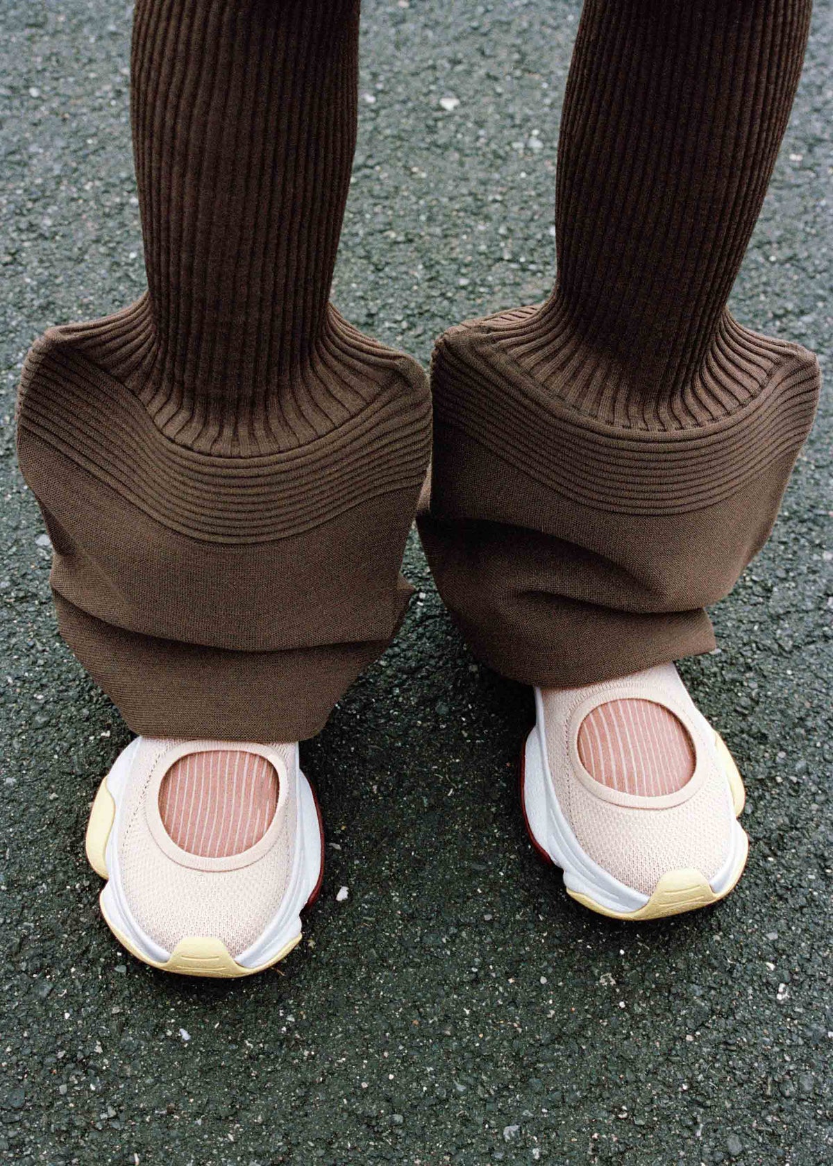 A person wearing wide, ribbed brown pants with long, flared legs that cover most of their ISSEY MIYAKE KARST FINCH sneakers, standing on a textured asphalt surface. view 13 of 18