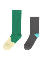 The KARST FINCH socks by ISSEY MIYAKE—one green with a cream toe, the other dark gray with a light blue heel—are shown side by side on a white background, perfect for pairing with colorful sneakers.