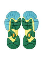 The chunky, segmented soles of the ISSEY MIYAKE KARST FINCH sneakers are seen from below, featuring blue, yellow, and green sections with black accents and a small orange hexagonal Vibram logo—reflecting their playful style.