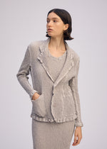 A person with short dark hair models the ISSEY MIYAKE WAVELET ENSEMBLE—a textured light gray skirt suit with a jacquard stretch tailored jacket, ruffled edges, and two buttons—posing sideways with one hand in a pocket against a plain background.