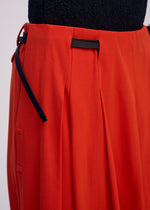 Close-up of a person wearing ISSEY MIYAKE's LOOPED bright orange pants with black details and a drawstring waist, paired with a textured black top.