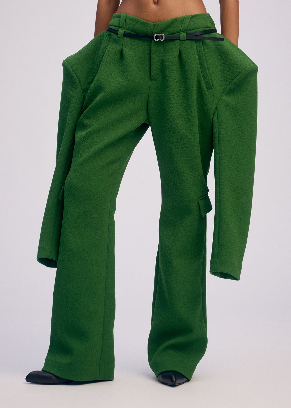 A person wearing ISSEY MIYAKE's ARMS pants—oversized green with extra-long, wide legs and jacket-like attached sleeves—shows only their torso and lower half. view 5 of 5