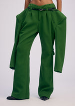 A person wearing ISSEY MIYAKE's ARMS pants—oversized green with extra-long, wide legs and jacket-like attached sleeves—shows only their torso and lower half.
