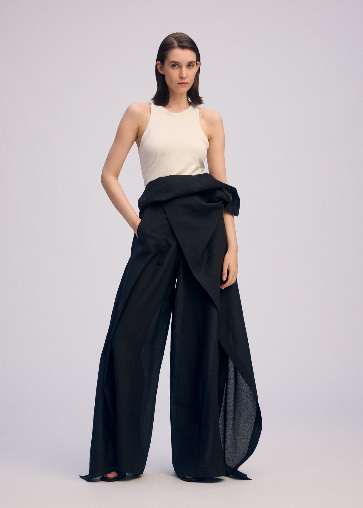 A woman with straight, shoulder-length hair and a neutral expression wears the ISSEY MIYAKE ALL SQUARES sleeveless white top and black high-waisted, asymmetrical draped pants against a plain background. view 7 of 8