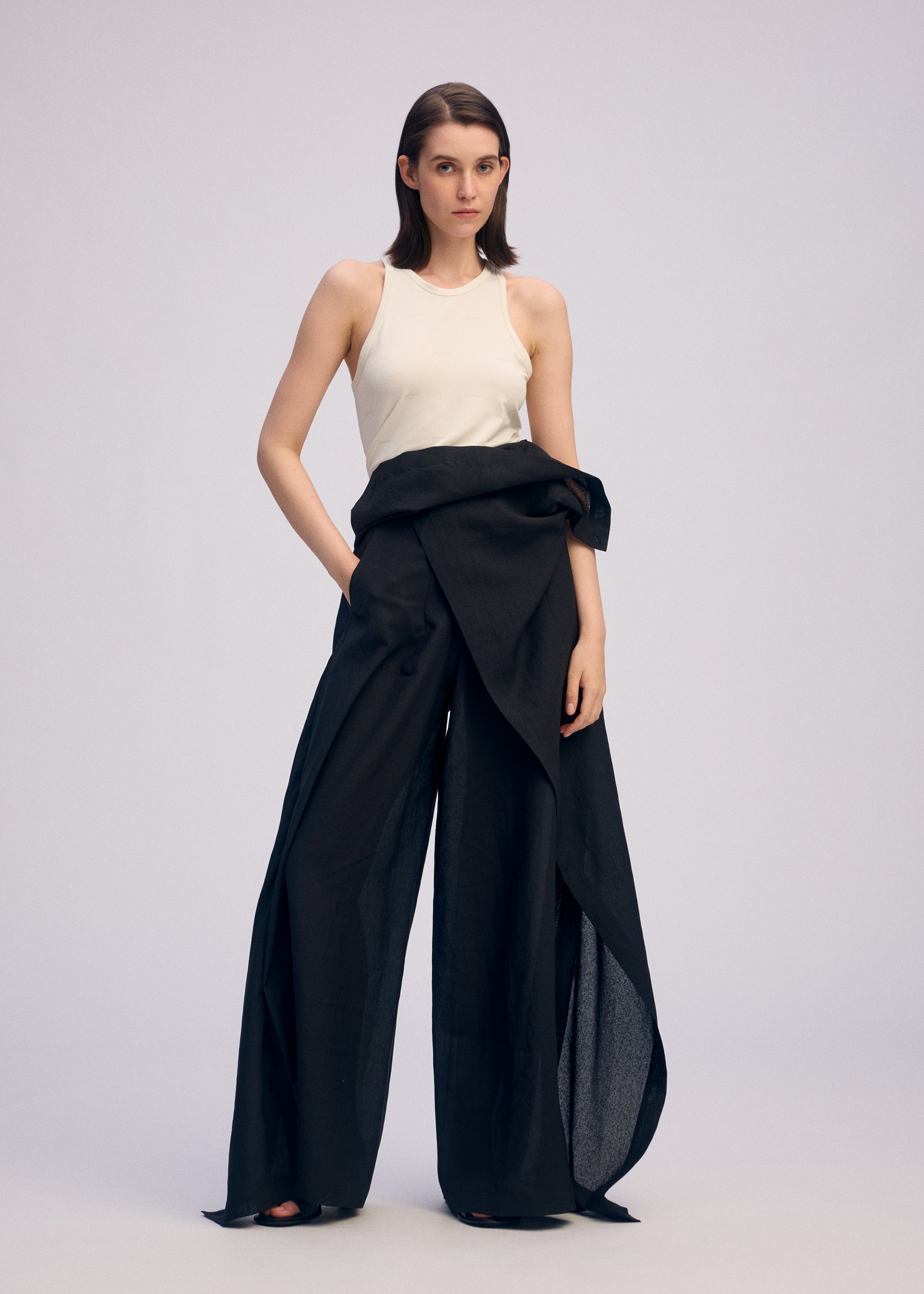 Zoomed view A woman with straight, shoulder-length hair and a neutral expression wears the ISSEY MIYAKE ALL SQUARES sleeveless white top and black high-waisted, asymmetrical draped pants against a plain background.