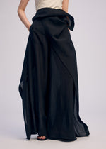 A person wears ISSEY MIYAKE’s ALL SQUARES wide-leg black wrap pants in ultra-fine polyester, paired with a sleeveless top; one hand is in the pocket. The image is cropped from shoulders down against a light background.