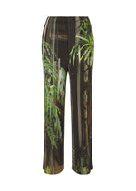 The ISSEY MIYAKE URBAN JUNGLE PLEATS are loose-fitting, ribbed pants with an elastic waistband, showcasing a tropical print of green palm leaves and brown vertical stripes. - BLACK-HUED （no.17）