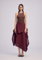 A woman with straight, shoulder-length dark hair stands facing forward, wearing a sleeveless brown top and the ISSEY MIYAKE ALL SQUARES asymmetrical burgundy skirt in ultra-fine polyester. She pairs it with black sandals against a plain light background.