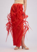 A model wears the URBAN JUNGLE skirt by ISSEY MIYAKE—long, bright red with dramatic sculptural spikes—paired with a beige sleeveless top and sandals, set against a plain light background.