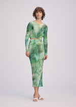 A woman wears the OBSCURE PLEATS dress by ISSEY MIYAKE, featuring green and white pleats.