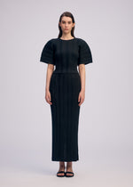 A woman faces forward in ISSEY MIYAKE’s LINEN LIKE RIB PLEATS: a fitted, ankle-length black dress with short structured sleeves and vertical ribbed details. She has straight brown hair and wears black sandals against a plain light background.