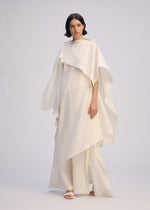 A woman with short dark hair wears the ALL SQUARES ensemble by ISSEY MIYAKE, crafted from ultra-fine polyester with wide, flowing sleeves and pants. She poses in white sandals against a plain, light background.
