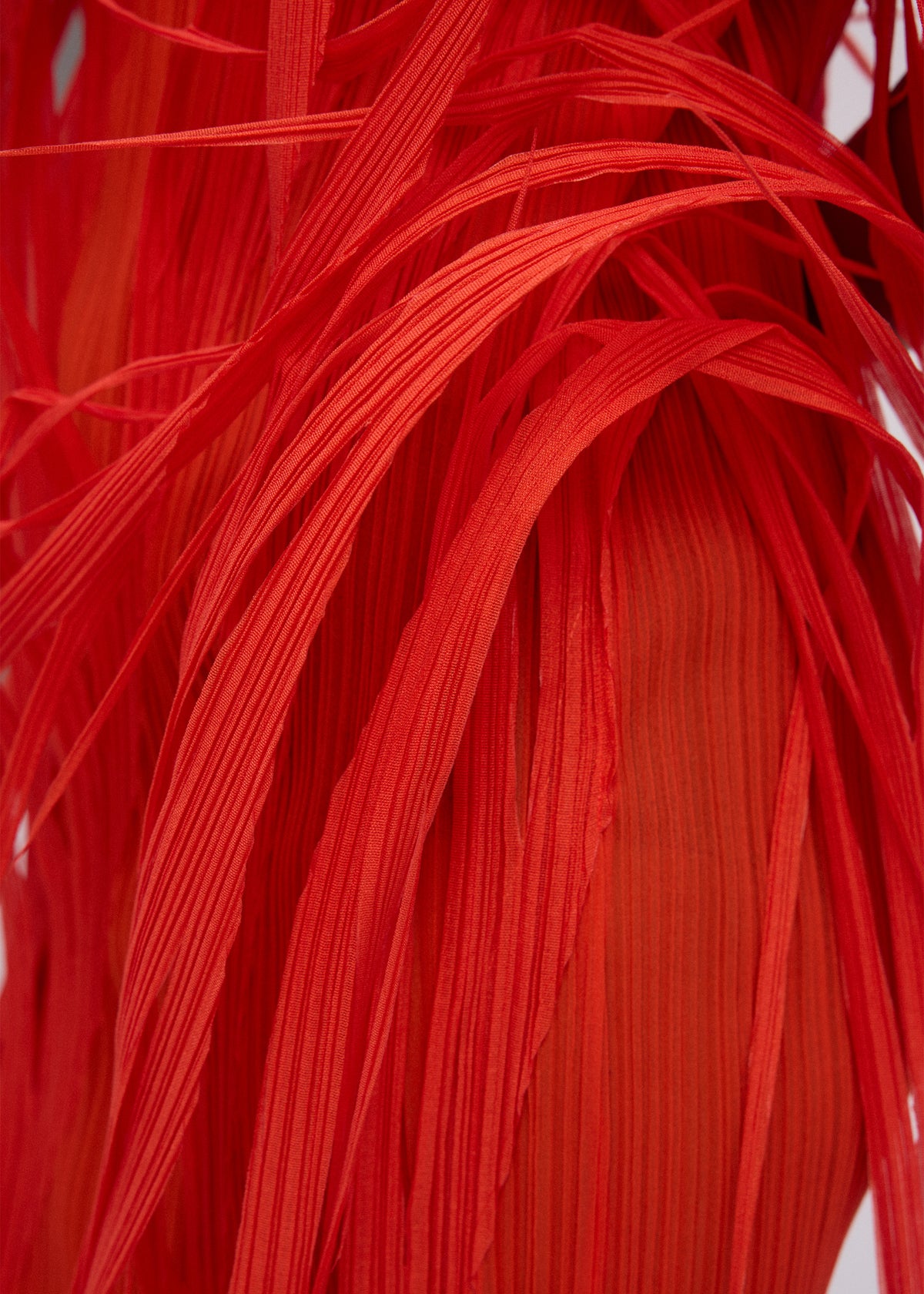 Close-up of URBAN JUNGLE by ISSEY MIYAKE: vibrant red, ribbed fabric with layered, ribbon-like strands overlapping to form a dynamic, abstract pattern. view 7 of 7