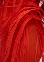 Close-up of URBAN JUNGLE by ISSEY MIYAKE: vibrant red, ribbed fabric with layered, ribbon-like strands overlapping to form a dynamic, abstract pattern.