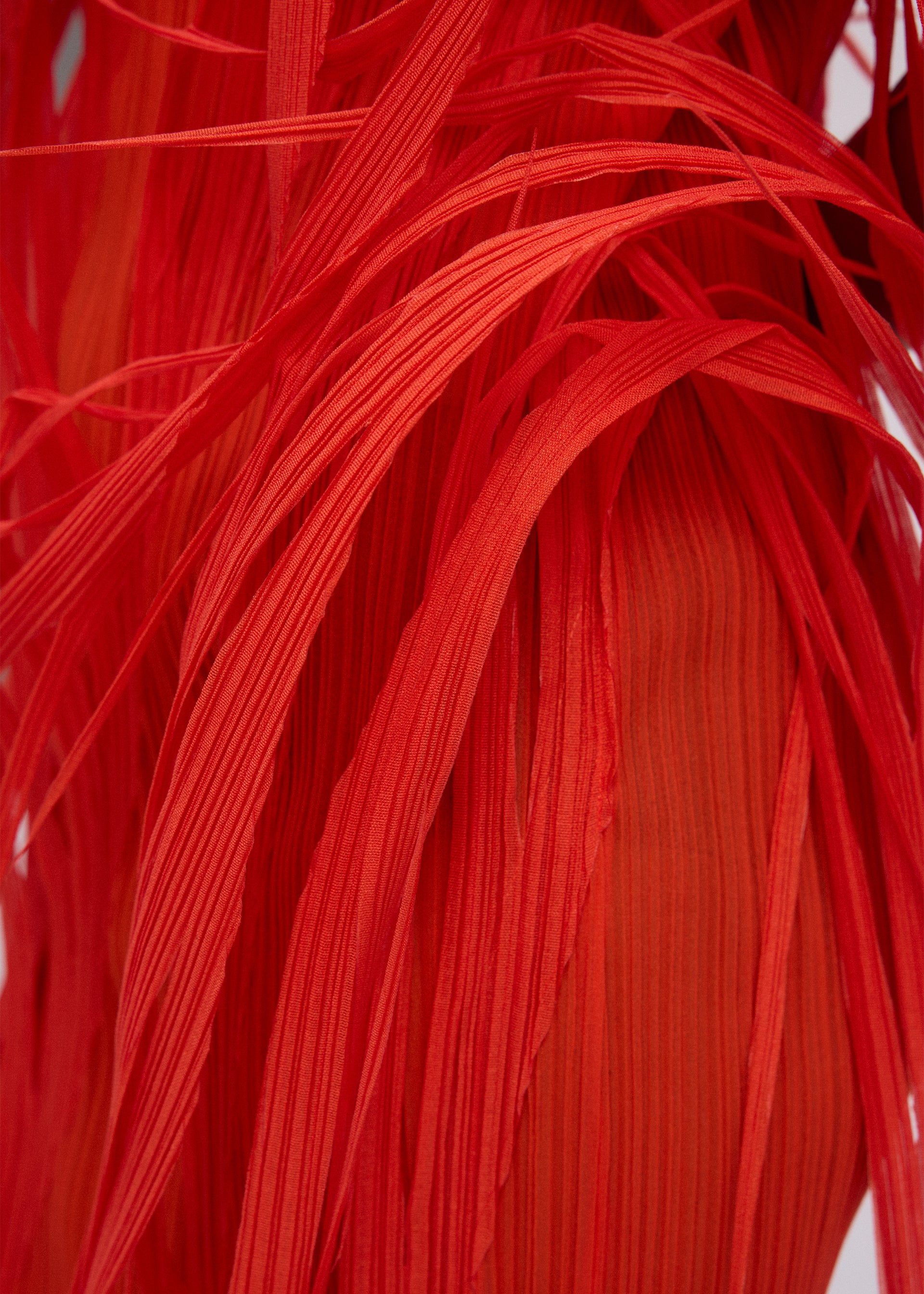 Zoomed view Close-up of URBAN JUNGLE by ISSEY MIYAKE: vibrant red, ribbed fabric with layered, ribbon-like strands overlapping to form a dynamic, abstract pattern.