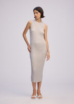 A woman poses against a light background wearing the ISSEY MIYAKE SLEEK PLEATS round-neck sleeveless, form-fitting textured light gray midi dress and white open-toe sandals, with one hand by her side and the other touching her hip.