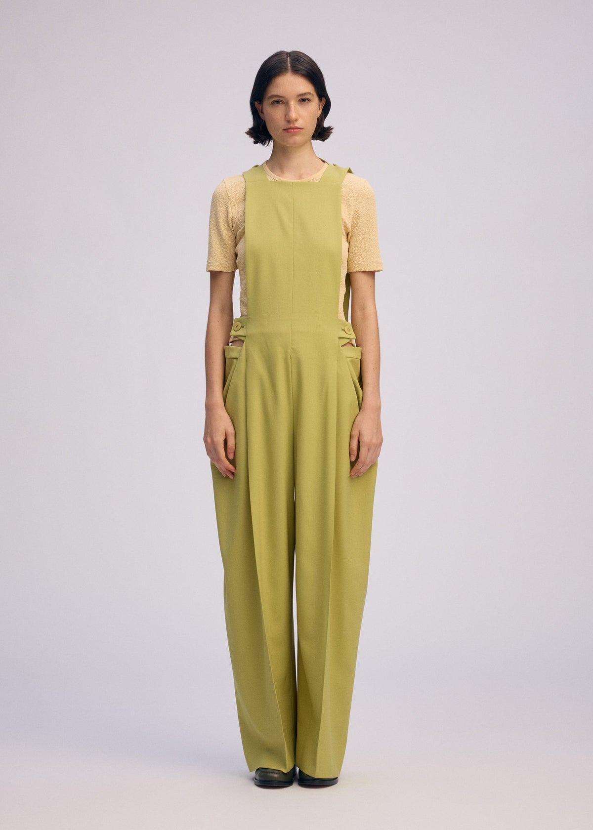 A woman faces forward in ISSEY MIYAKE BELTED WOOL PANTS with wide legs, paired with a short-sleeve beige top and black shoes. She has short dark hair, a neutral expression, and stands against a plain light background. view 5 of 7