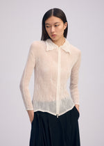 A person with long dark hair wears the ISSEY MIYAKE CHIFFON TWIST BK/WT-66, a sheer, textured white zip-up cardigan with a collar made from recycled polyester, and loose black pants, standing against a light background.