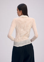 A person with long, straight dark hair is seen from behind wearing the ISSEY MIYAKE CHIFFON TWIST BK/WT-66—a sheer, pleated cream top with loose black pants—against a plain light background.