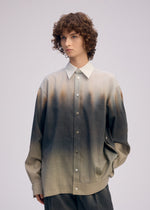 A person with curly brown hair models the ISSEY MIYAKE PLUMAGE set—an oversized artisan shirt and matching loose-fit pants with a gradient feather pattern from beige to dark gray—against a plain light background.