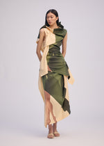 A woman poses against a plain light background wearing the BODY AT PLAY sleeveless draped dress by ISSEY MIYAKE in green and beige with an original pattern. She has long, straight dark hair and nude sandals.