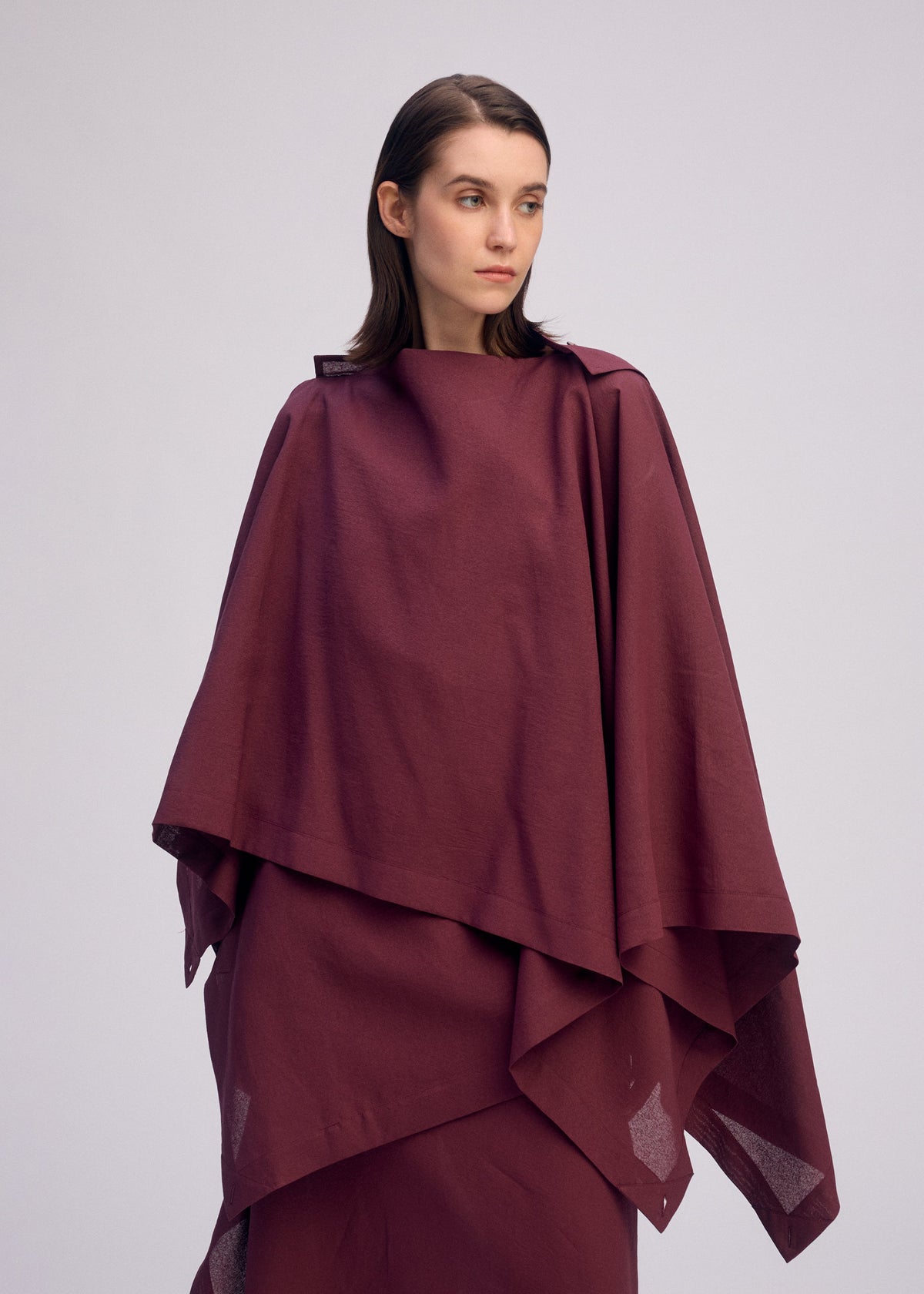 A woman with straight brown hair wears a loose-fitting, layered maroon ALL SQUARES top by ISSEY MIYAKE and looks to the side against a plain light background. view 7 of 8