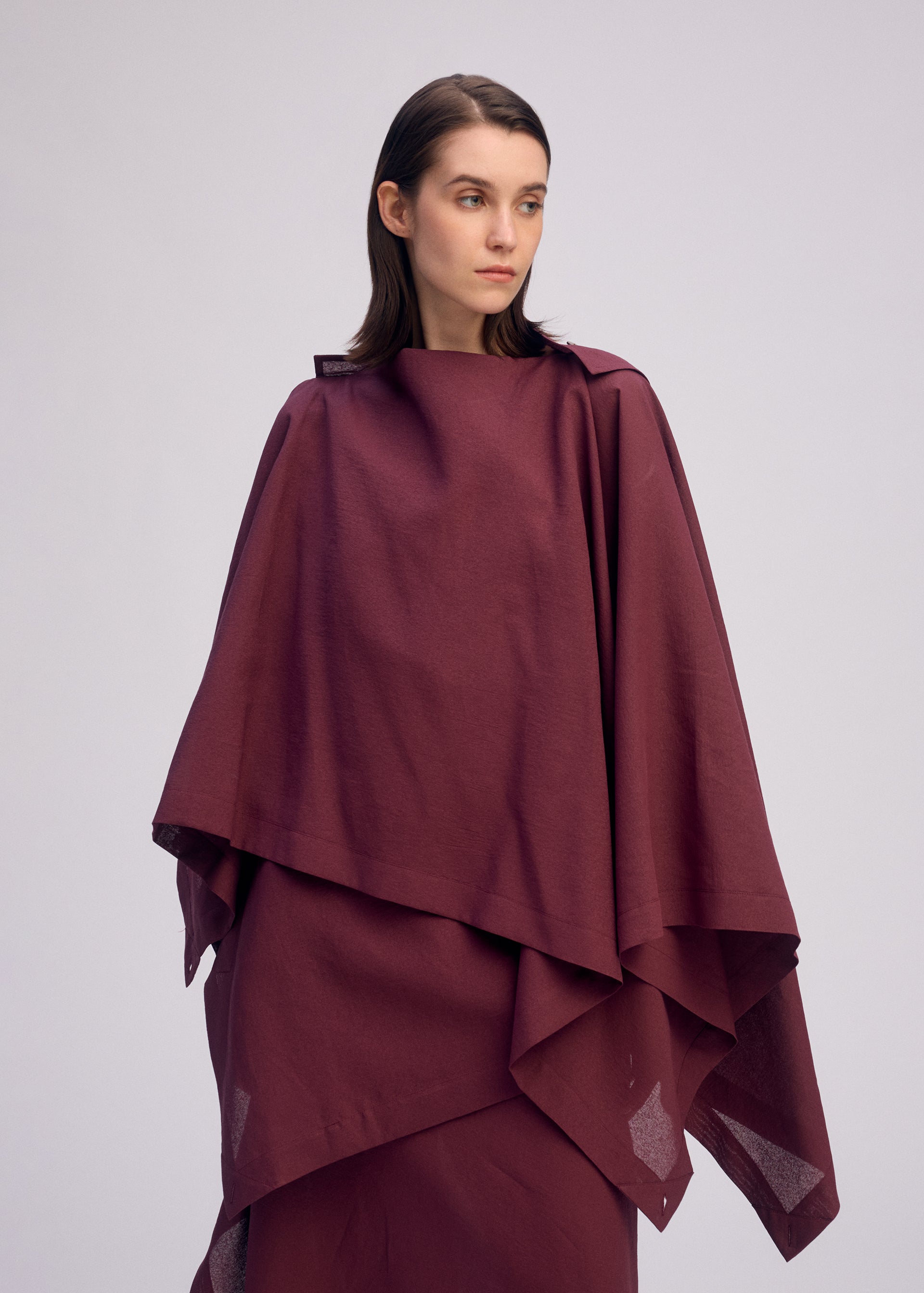 Zoomed view A woman with straight brown hair wears a loose-fitting, layered maroon ALL SQUARES top by ISSEY MIYAKE and looks to the side against a plain light background.