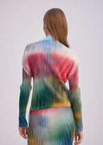 A person with straight brown hair is seen from behind, wearing ISSEY MIYAKE’s OBSCURE PLEATS long-sleeved ribbed dress featuring a moiré-patterned top in red, blue, green, and yellow tones against a plain background.