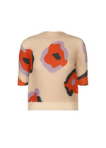 The VERVE PLEATS TOP by ISSEY MIYAKE is a beige, short-sleeved boat-neck top with bold red, black, and lavender abstract floral prints. Its loose fit and textured fabric make it perfect for everyday wear. - BEIGE-HUED （no.46）