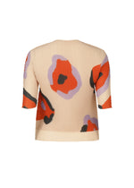 The VERVE PLEATS TOP by ISSEY MIYAKE is a beige, short-sleeved boat-neck top with pleats and bold red, black, and lavender floral abstract patterns—perfect for everyday style.