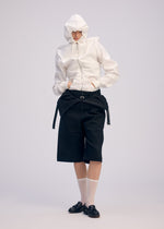 A person poses against a plain background in ISSEY MIYAKE's GENERIC WEAR: a playful hoodie with a white hood, black knee-length shorts, sheer white socks, and black loafers, hands tucked in pockets.