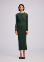 A person stands facing forward, wearing the ISSEY MIYAKE RHOMBUS PLEATS ribbed, long-sleeve, button-up dark green top and matching ankle-length skirt with black sandals against a plain light background.