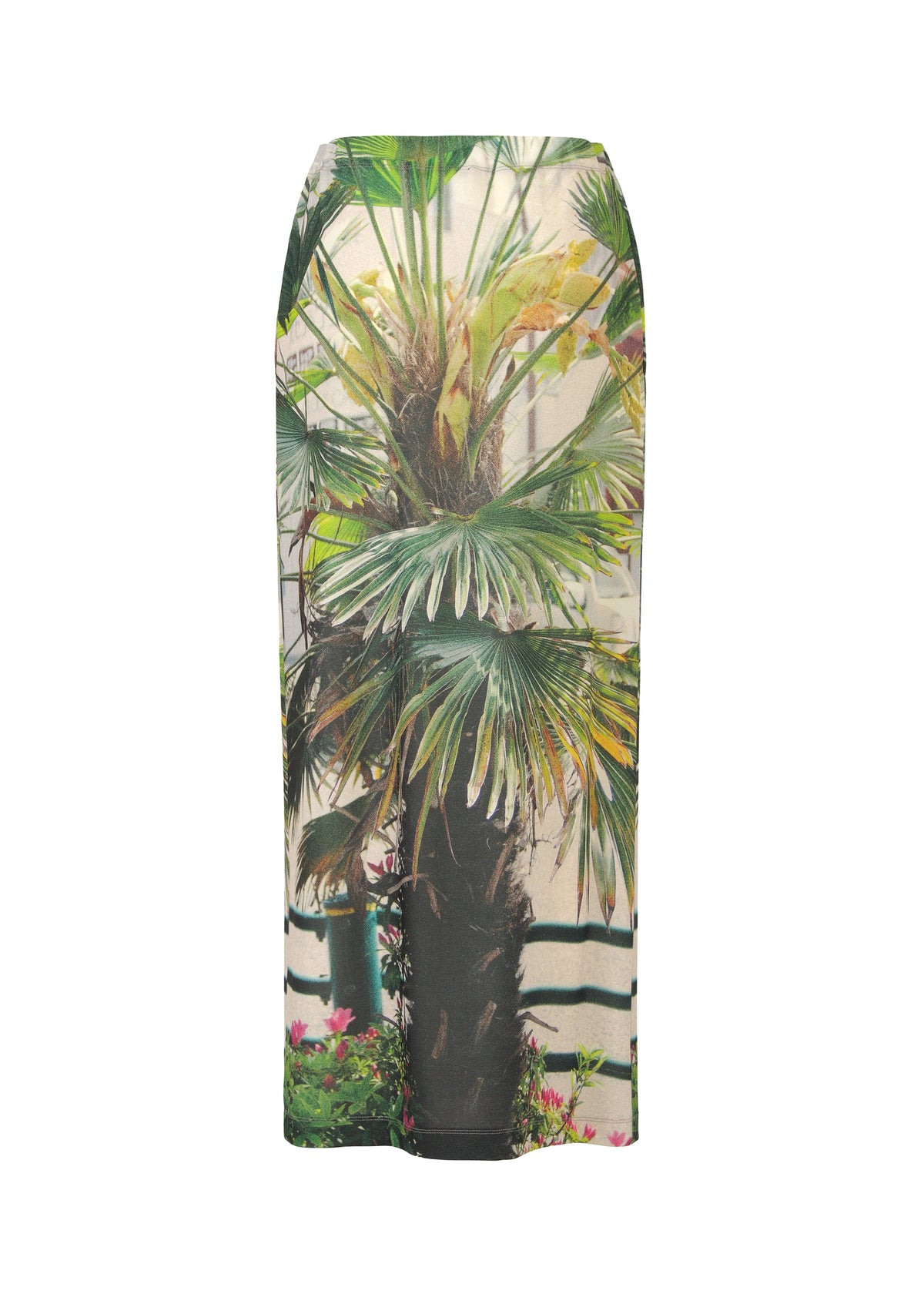 The URBAN JUNGLE JERSEY by ISSEY MIYAKE is a fitted long skirt showcasing a lifelike palm plant design with a brown trunk, light background, and accents of railing and foliage along the hem. view 3 of 7