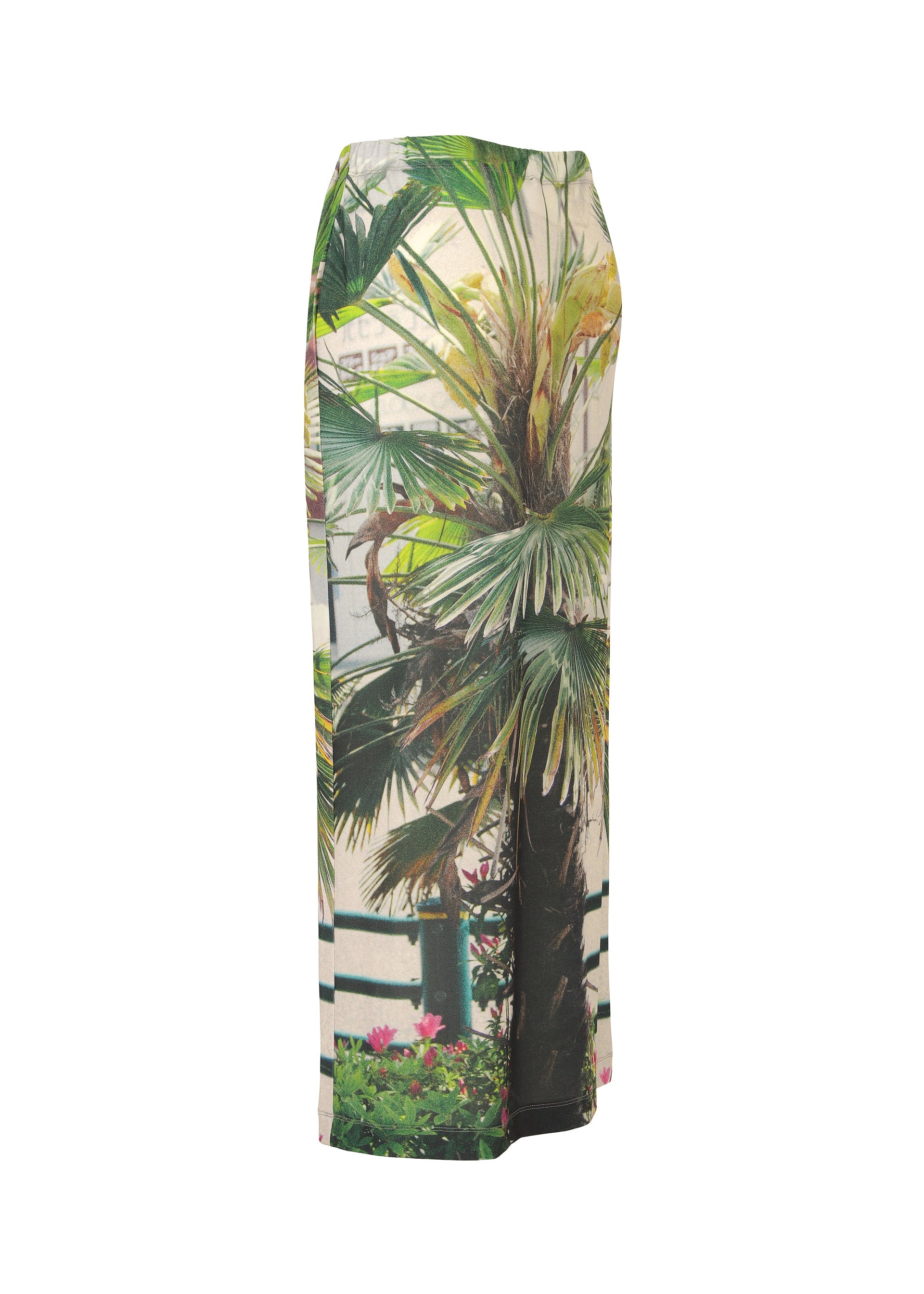 Zoomed view The ISSEY MIYAKE URBAN JUNGLE JERSEY is a long skirt with a bold palm plant print featuring green foliage, floral accents, and a fence motif, shown against a white background.