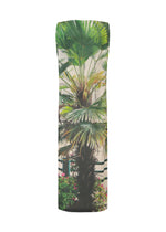 The URBAN JUNGLE JERSEY by ISSEY MIYAKE is a sleeveless dress with a jungle greenery print of palm fronds and foliage on a light background, accented with pink flowers at the base.